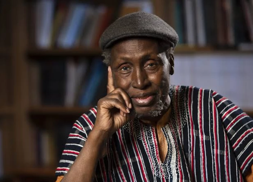 A dignified portrait of Ngũgĩ wa Thiong'o, a dark-skinned man with short, grey hair, wearing glasses, looking thoughtfully towards the viewer.