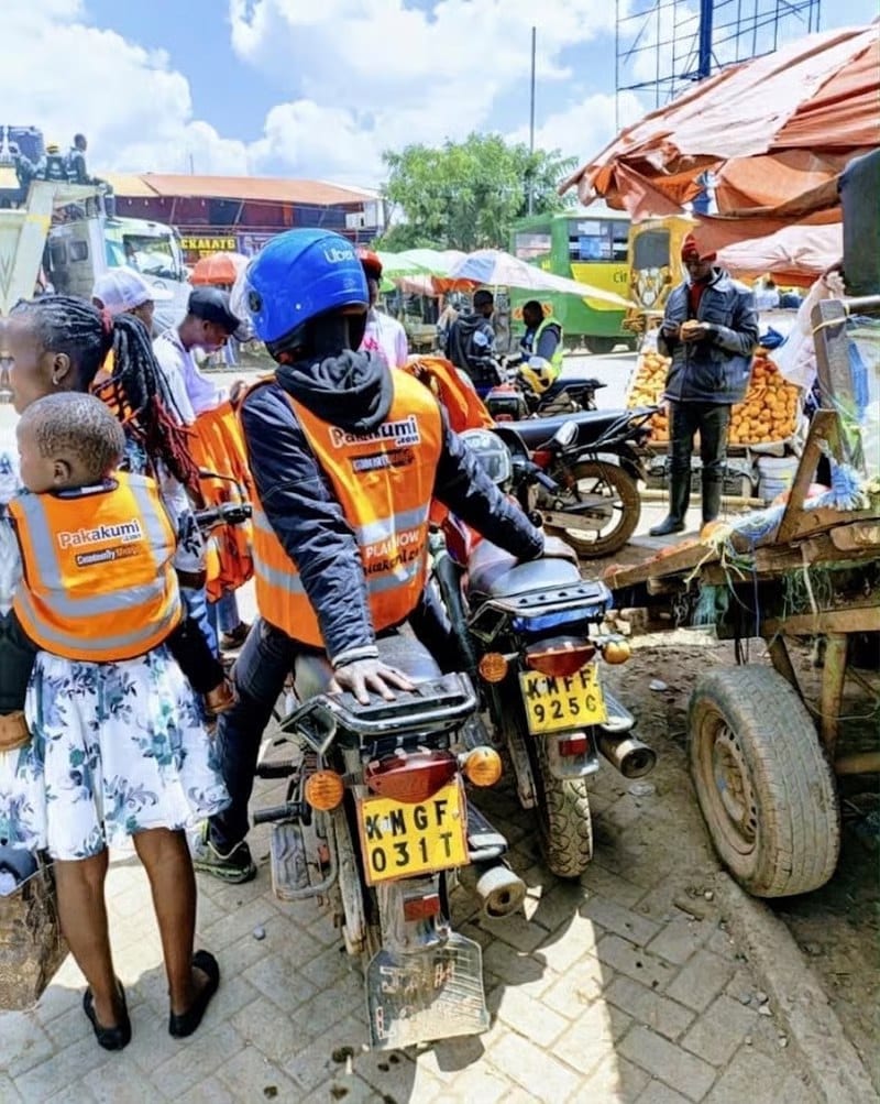 A child carried on her mother's back with a branded reflector vest handed out at a Pakakumi roadshow.