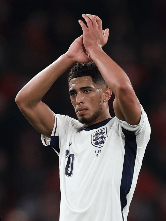 An image of Jude Bellingham celebrating after scoring a goal for Real Madrid, wearing the iconic white jersey and raising his arms to a...